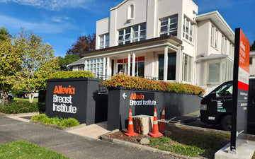 Exterior view of Allevia Breast Institute featuring prominent dual wall signs with directional wayfinding and brand-colour logo application