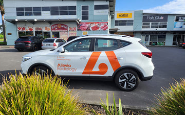 White SUV with Allevia Radiology branding and orange logo, parked outside shops, promoting mobile healthcare services and medical imaging visibility.