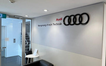 Audi reception area wall featuring 3D logo with four rings and the brand slogan ‘Vorsprung durch Technik’ in black and red lettering