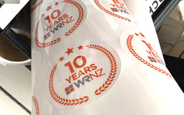 Roll of circular WRNZ 10-year anniversary stickers with red laurel design, printed to celebrate a decade of business success.