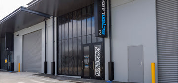 Front view of Faction Labs at unit 3, featuring a dark glass facade with graphic artwork, prominent vertical signage, and a door labeled “Refuse to Be Ordinary.”