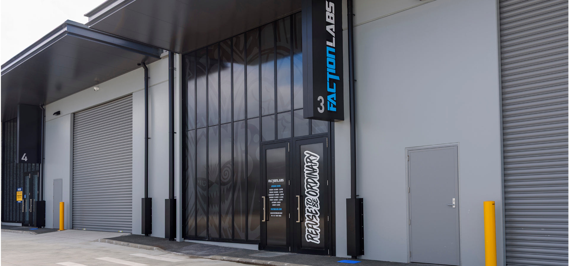 Front view of Faction Labs at unit 3, featuring a dark glass facade with graphic artwork, prominent vertical signage, and a door labeled “Refuse to Be Ordinary.”