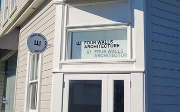 Exterior of Four Walls Architecture featuring a round blade sign and upper window graphics with bold black logo and company name