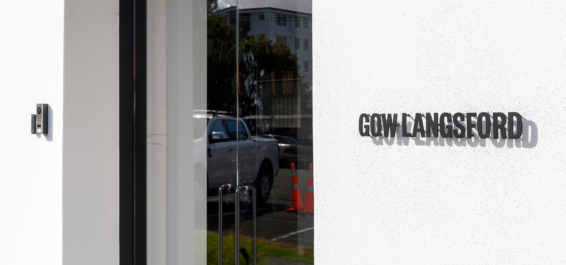 Modern glass entrance with minimalist signage for Gow Langsford Gallery, reflecting parked vehicles and surrounding architecture.