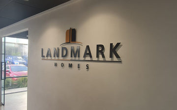 Interior office wall signage for Landmark Homes featuring 3D logo and lettering in black and bronze tones with sleek, professional finish