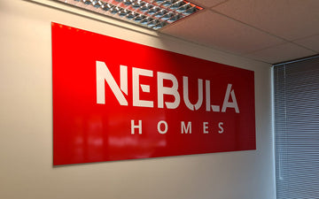 Interior wall signage for Nebula Homes featuring bold red background and white cut lettering in a modern office space
