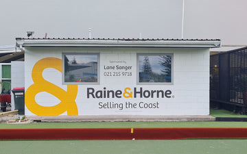 Bold outdoor wall signage for Raine & Horne featuring large ampersand symbol, company branding, and sponsor details for Lane Sanger