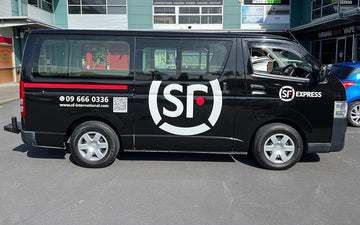 Black SF Express delivery van with bold white and red logo, contact number, and QR code for international courier services, parked outside commercial buildings.