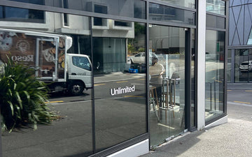 Minimal white vinyl logo for ‘Unlimited’ applied to street-facing glass doors and windows of a modern office or retail space