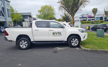 White ute with VSL Landscapes branding parked in front of company signage, representing professional landscape maintenance and gardening services.