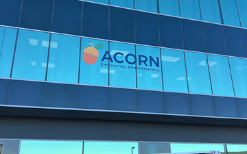 Window signage featuring the ACORN logo with acorn icon and the tagline ‘Embracing Neurodiversity’ on a modern glass office facade