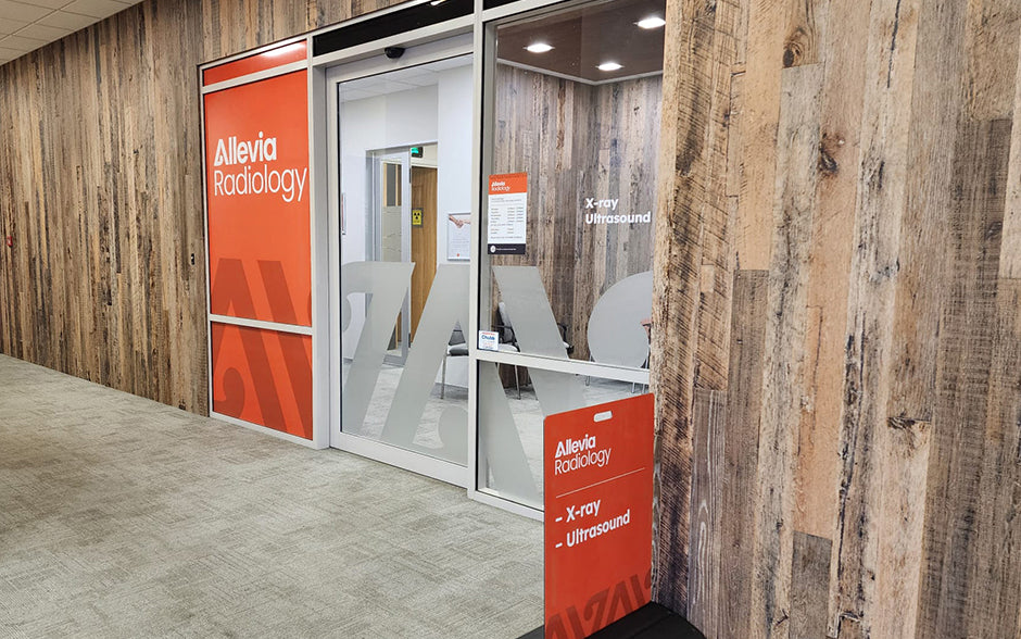 Allevia Radiology clinic interior entrance featuring frosted vinyl glass doors, bold wall branding, and a red footpath sign listing X-ray and Ultrasound services