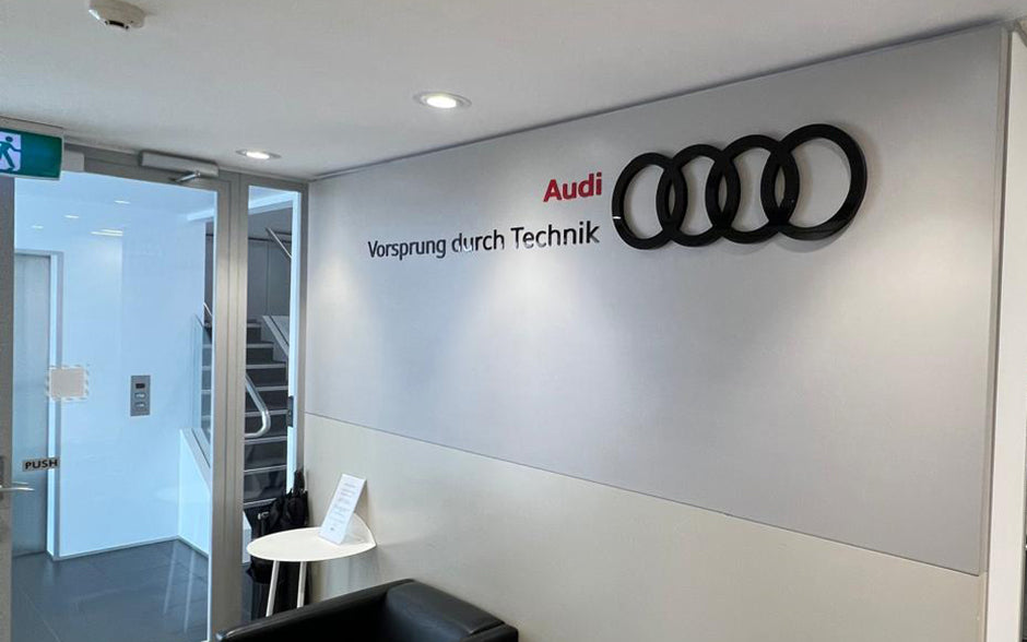 Audi reception area wall featuring 3D logo with four rings and the brand slogan ‘Vorsprung durch Technik’ in black and red lettering