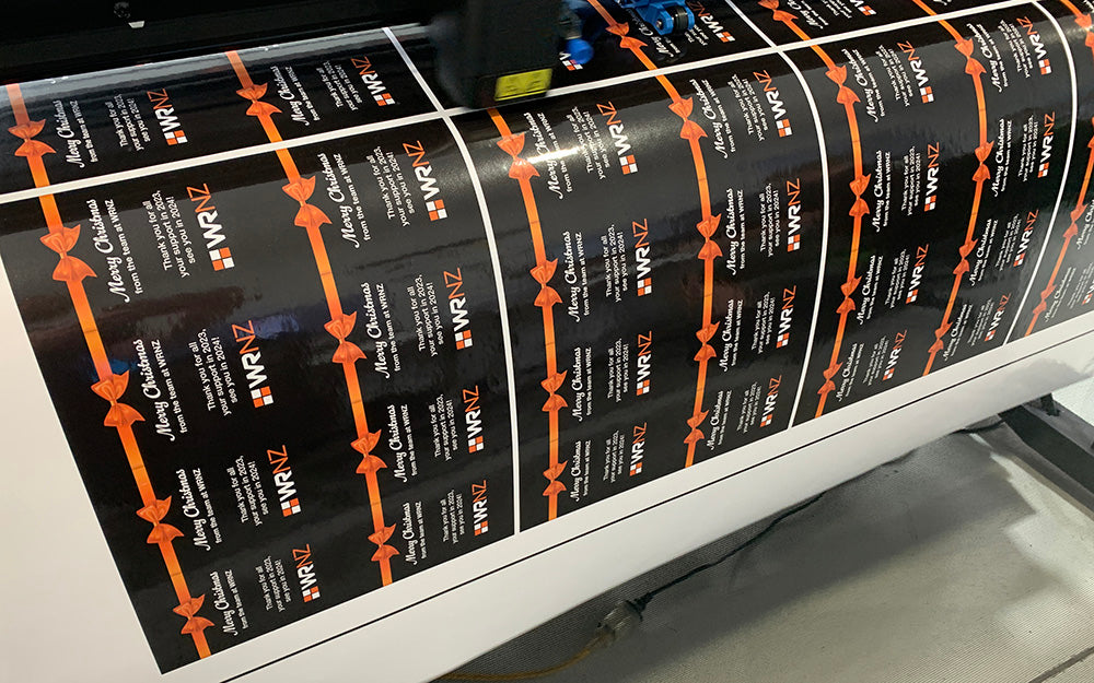 Black and orange custom WRNZ holiday labels being printed, featuring festive design with bows and Christmas message for client gifts.