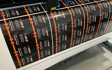 Black and orange custom WRNZ holiday labels being printed, featuring festive design with bows and Christmas message for client gifts.