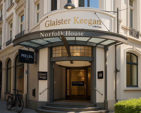 Front entrance of Glaister Keegan Lawyers at 18 Norfolk House, featuring a curved glass awning, gold signage, and a bicycle near a café sign.