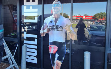 Large window graphic at Nutrition Warehouse featuring an athlete in branded gear alongside bold vertical text ‘Built for Life’