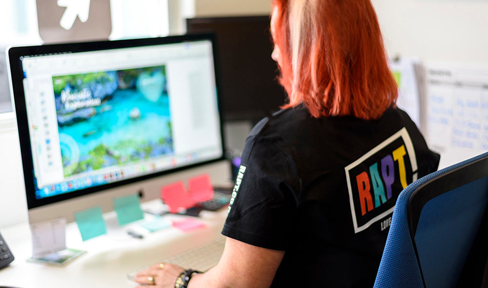 RAPT staff member working on a digital design project at a desktop computer, showcasing creative layout skills and vibrant branding in a studio environment.