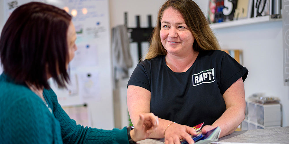 RAPT team member presenting a selection of printed product samples to a customer in a friendly, personalised consultation setting.